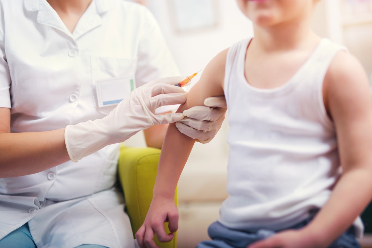 Vakcinacija deteta - doktor vakciniše dete - dete sedi i doktor mu daje injekciju u ruku.