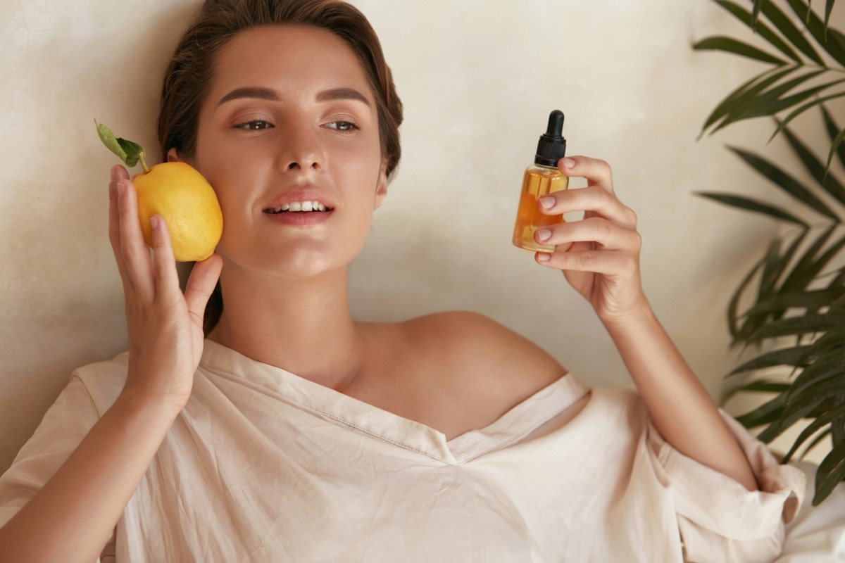 Žena s citrónom a fľaštičkou s výťažkom vitamínu C v ruke, vitamín, ktorý pomáha pokožke