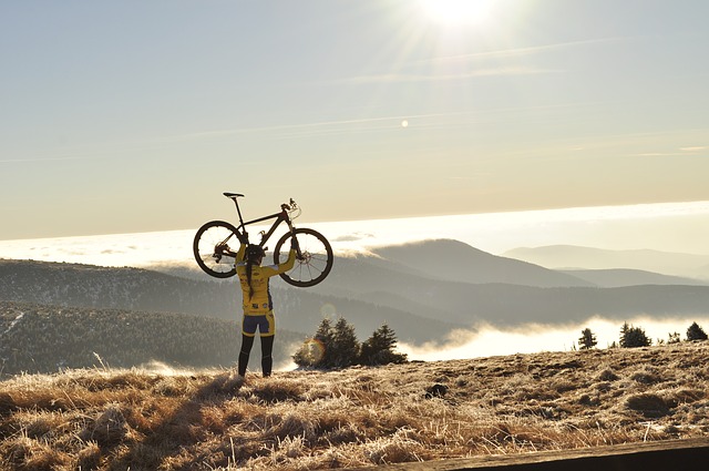 Cyklistka dvíha nad hlavu bicykel. V pozadí sú hory v hmle.