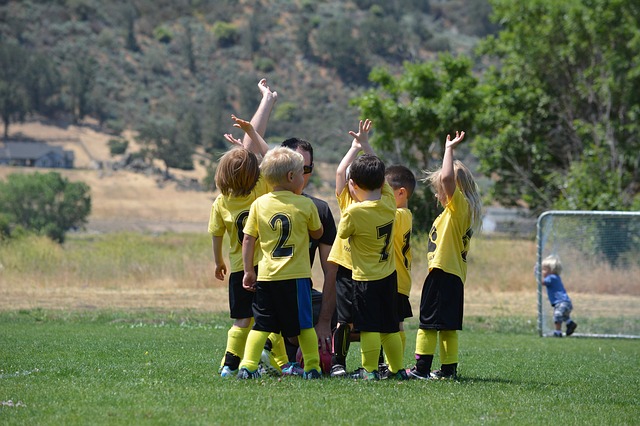 Deti v žltých dresoch na futbalovom ihrisku. Tešia sa v hlučiku spolu so svojim trénerom.