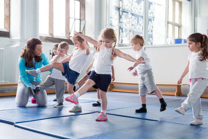 Malé deti v telocvični, precvičujú s učiteľkou.