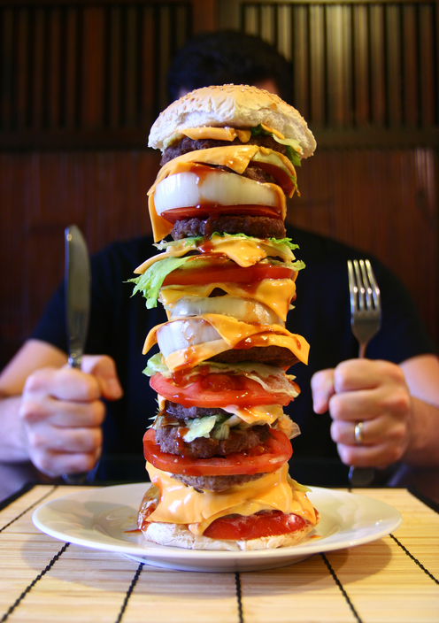 Muškarac sedi za stolom, na tanjiru ima visok hamburger, megaporcija