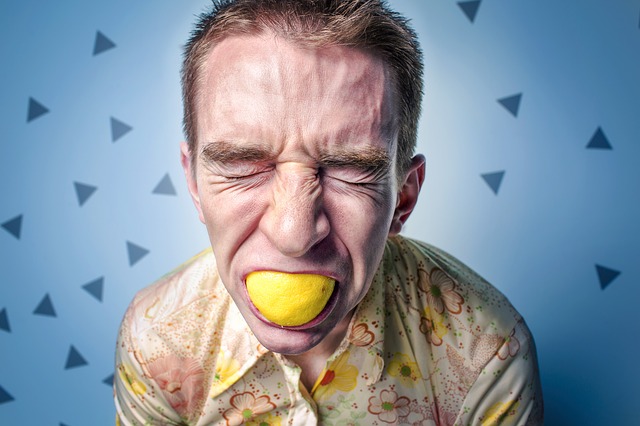 čovek sa limunom u ustima ima kiselkast izraz lica, moguća alergijska reakcija na citruse